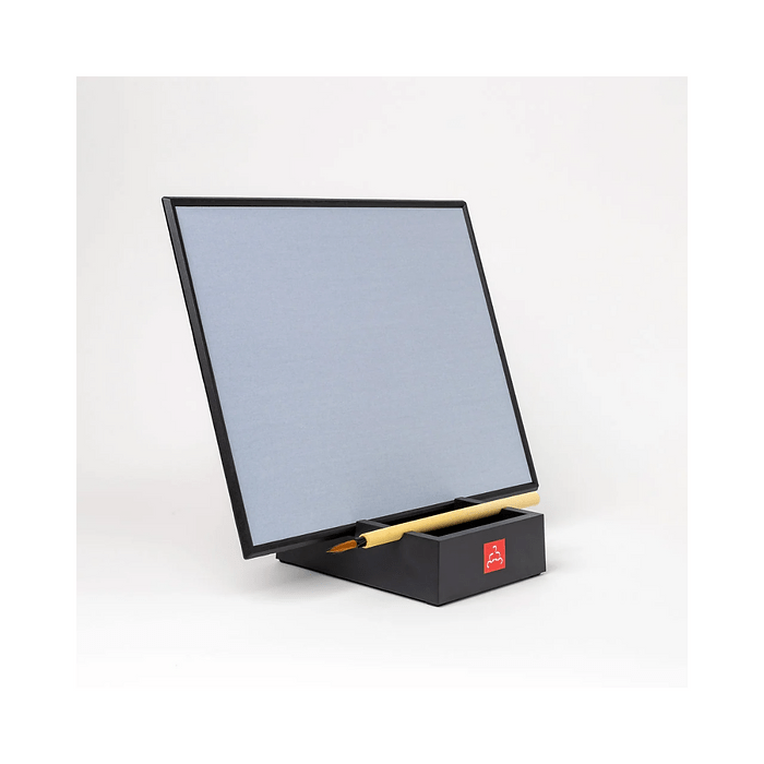 Black Buddha Board with a light gray surface, propped up at an angle on a black base. The base includes a red Buddha Board logo and holds a bamboo water brush. The background is plain white, highlighting the minimalist and elegant design of the Buddha Board.