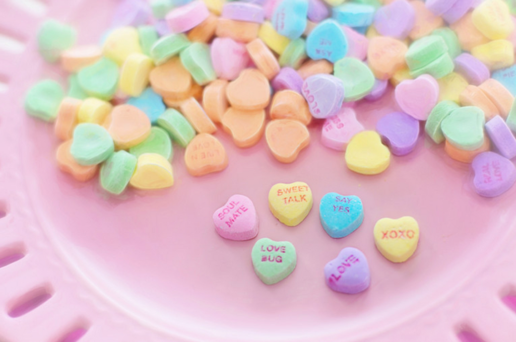 Colorful conversation heart candies on a pink plate, symbolizing the mixed emotions of navigating the holidays as a newly single person and embracing self-love and new traditions.