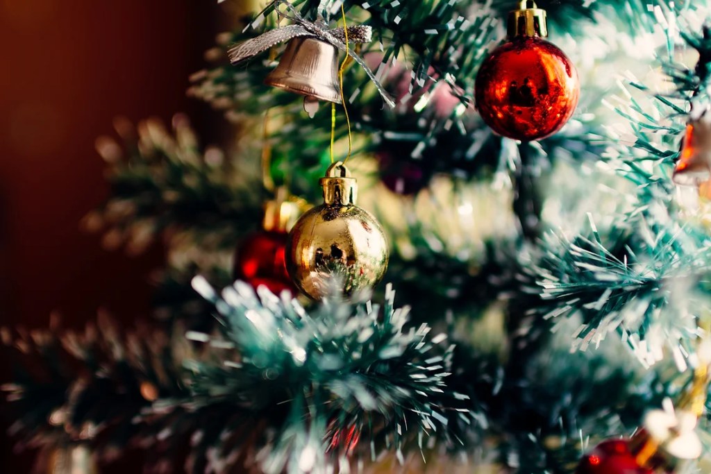 Close-up of Christmas tree decorated with red and gold baubles, symbolizing the chaotic yet joyful essence of surviving the holiday season with humor and lowered expectations.