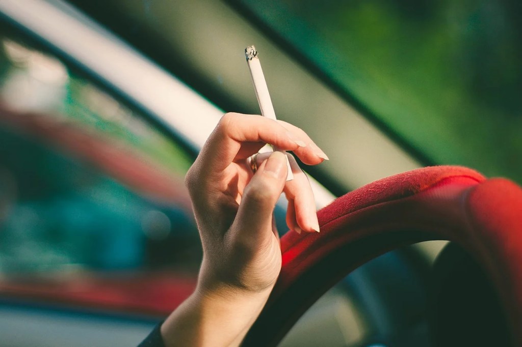 Hand holding a cigarette while driving, highlighting the link between stress and unhealthy coping mechanisms like smoking.