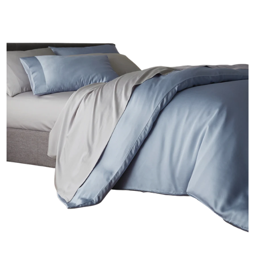 A bed featuring light blue silk bedding and pillows, elegantly draped over a gray upholstered bed frame.