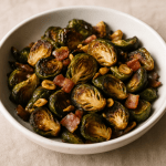 A white bowl filled with roasted Brussels sprouts, crispy pancetta pieces, and golden toasted garlic slices, all caramelized and glossy under warm light.