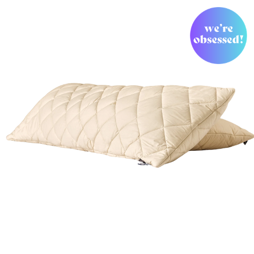 Two cream-colored, quilted pillows from Woolroom stacked on top of each other, with a circular graphic in the top right that says 'we're obsessed!'