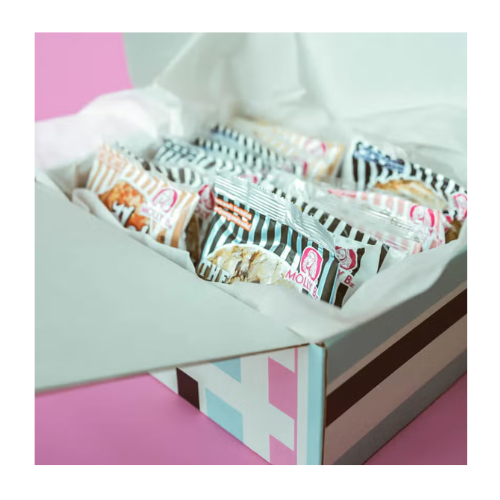 A opened box containing several packets of snacks from Molly Bz's, arranged neatly inside with a pink background.