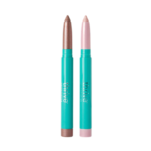 Two makeup crayons from Thrive Cosmetics, one in a shimmering bronze shade and the other in a soft pink shade, both with turquoise packaging.