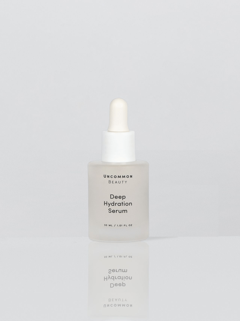 A dropper bottle of Uncommon Beauty Deep Hydration Serum, 30 mL, with a matte white finish and a bulb dropper cap, set against a minimalist background.